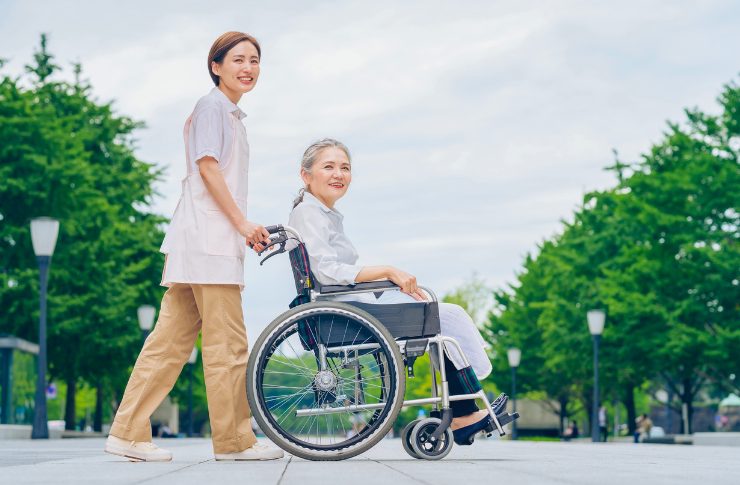 笑顔の高齢女性の車を椅子をおす介護士