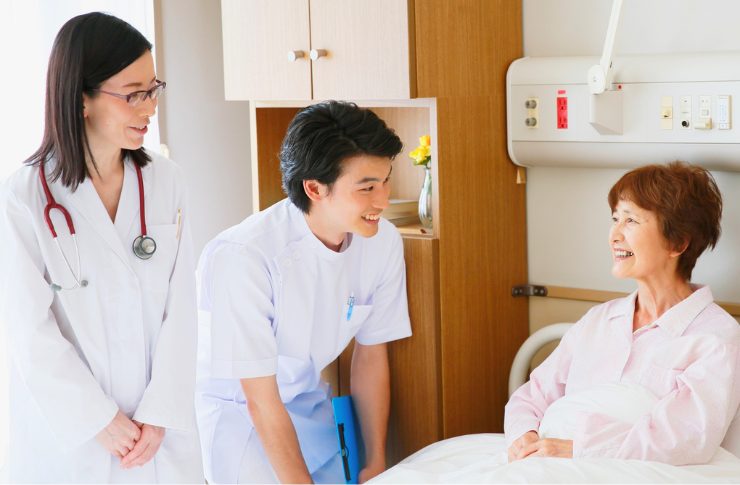 ベッドに座る患者と談笑する女医と男性介護士